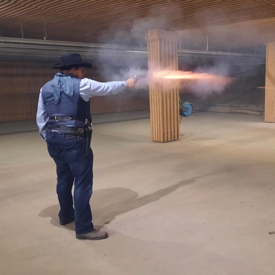 Cowboy Action Shooting: Schütze im Westernkostüm mit Mündungsfeuer aus dem Revolver